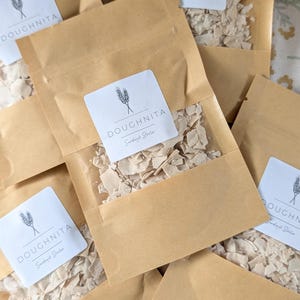 May include: Multiple brown paper bags with white labels that say "DOUGHNITA Sourdough Starter" and contain white sourdough starter pieces.