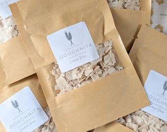 May include: Multiple brown paper bags with white labels that say "DOUGHNITA Sourdough Starter" and contain white sourdough starter pieces.