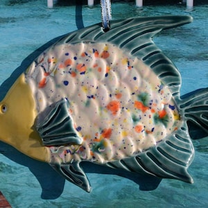 May include: A ceramic fish ornament with a yellow head, teal fins, and a white body with colorful splatter paint.