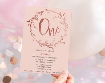 May include: A pink invitation card with a rose gold floral wreath and the number "One" in the centre. The text reads "Please join us for Amelia's 1st Birthday Celebrations Saturday 15th March at 2:00PM - 5:00PM 123 Leopold Hotel Livingston Street London ILH BH Please RSVP to Sarah on XXXXX XXXXX".