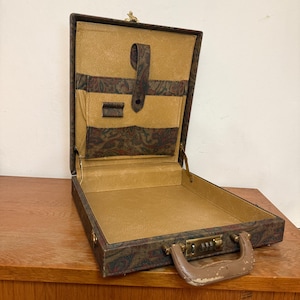 Könnte beinhalten: Geöffnete Vintage-Aktentasche mit braunem Paisley-Muster auf der Außenseite und beigefarbenem Innenraum. Die Aktentasche hat ein Zahlenschloss, einen Griff und Innentaschen. Der Koffer ist geöffnet und gibt den Blick ins Innere frei.
