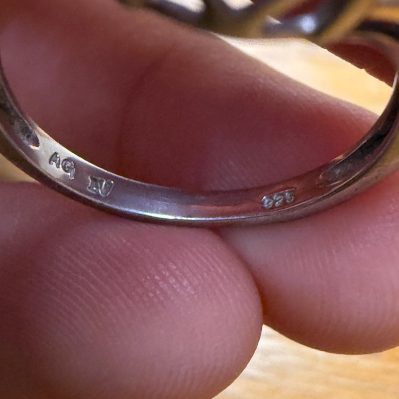 May include: Close-up of a silver ring with the markings "AG IV" and "925" visible. The ring is held by a person. The ring appears to be made of sterling silver.