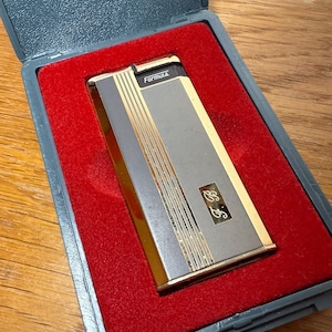 May include: A vintage Formula lighter in a gray case with a red velvet interior. The lighter is silver and gold with vertical gold stripes and the initials "E.F." The word "Formula" is printed on the top.