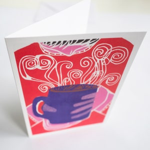 May include: A red and pink greeting card with a purple mug and white steam swirls. The mug is filled with a brown liquid.