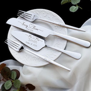 May include: A set of stainless steel cutlery including two forks, a knife, and a cake server, all featuring custom engravings. The knife is engraved with "Terry & Bria" and "10 18 2025", while the server reads "Mr & Mrs Smith" and "October 18 2025".
