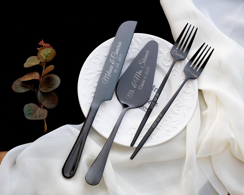 May include: A set of matte black stainless steel cake serving utensils including a knife, a cake server, and two forks. The knife is engraved with "Melanie & Cameron 10.04.2025", the server with "Mr. & Mrs. Skinner October 4, 2025", and the forks with names.
