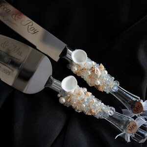 May include: A set of two silver cake knives with white and gold shell and pearl embellishments. The handles are decorated with the words "Mr." and "Mrs." and the blade has the text "Erica & Roy" engraved on it.