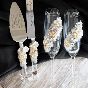 May include: A wedding cake cutting set with a silver knife and two champagne flutes decorated with seashells and starfish. The knife has the text "Mr. & Mrs. Lowe Jr. September 7, 2025" engraved on the blade. The flutes have the text "Mr. Lowe Jr. 07.07.2025" and "Mr. Lowe 09.07.2025" engraved on them.