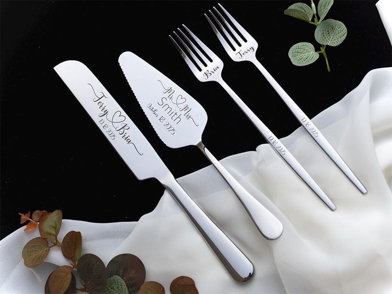 May include: A set of stainless steel wedding cake serving utensils including a knife, a cake server, and two forks. The knife is engraved with Terry & Bria 10.18.2025, the server with Mr & Mrs Smith October 18 2025, and the forks with Bria, Jerry, and 10.18.2025.