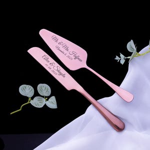 May include: A rose gold cake knife and server set featuring engraved text. The knife reads Alex & Shayla 11.08.2025 and the server reads Mr. & Mrs. Huffman November 8, 2025. The utensils have a metallic finish and are positioned on white fabric.