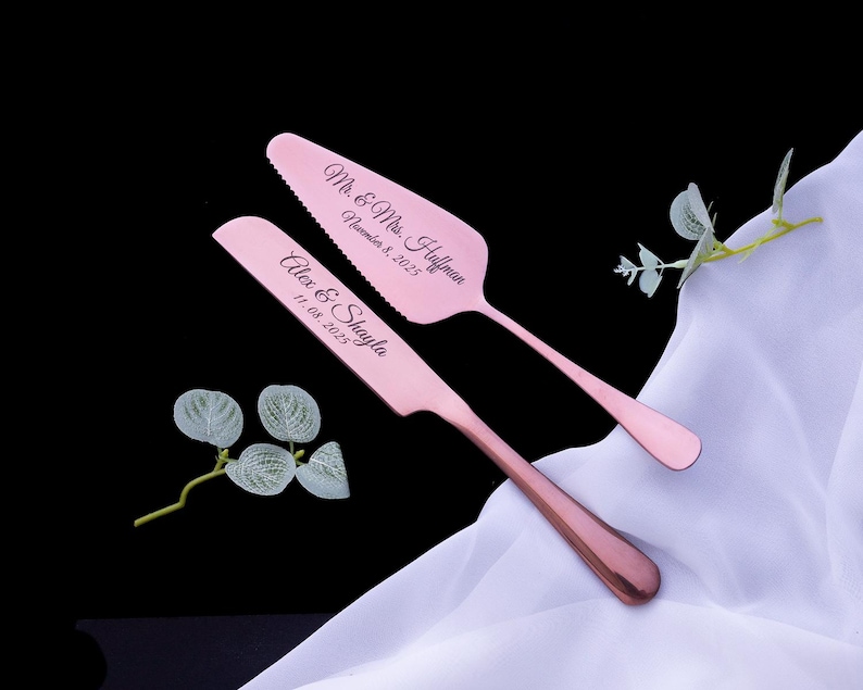 May include: A rose gold cake knife and server set featuring engraved text. The knife reads Alex & Shayla 11.08.2025 and the server reads Mr. & Mrs. Huffman November 8, 2025. The utensils have a metallic finish and are positioned on white fabric.