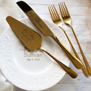 May include: A gold-toned cake serving set consisting of a serrated cake knife and a cake server, alongside two forks. The knife and server are engraved with "Mr & Mrs Sullivan May 4, 2024" and "Kyle & Chianne 5.4.2024". A white plate features the same text.