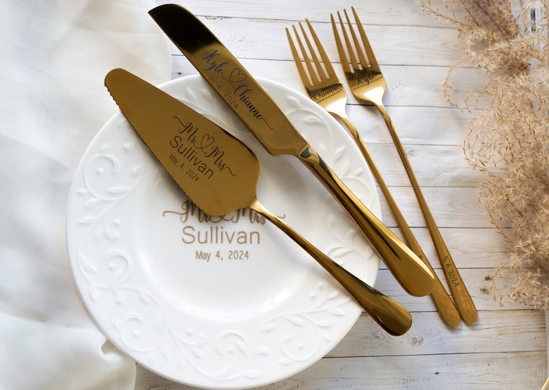 May include: A gold-toned cake serving set consisting of a serrated cake knife and a cake server, alongside two forks. The knife and server are engraved with "Mr & Mrs Sullivan May 4, 2024" and "Kyle & Chianne 5.4.2024". A white plate features the same text.