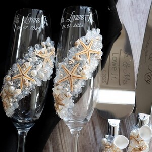 May include: Two champagne flutes decorated with seashells and starfish, with the text "Mr. Lowe Jr. 06.07.2025" and "Mrs. Lowe Jr. 06.07.2025" engraved on the glasses. A silver cake knife with the text "Rebecca & Jay Mr. & Mrs. Lowe Jr. 06.07.2025" is also included.