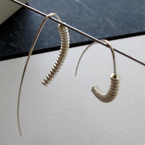 May include: A pair of silver earrings with a unique, coiled design. The earrings are hanging from a wire stand.