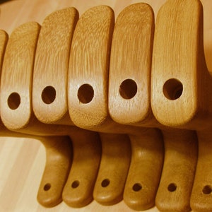 May include: Seven wooden handles with a hole in the centre, arranged in a row. The handles are a light brown colour and have a smooth finish.