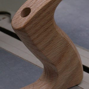 May include: A wooden handle with a curved shape and two holes. The handle is light brown in colour and has a smooth finish. The text "A110" is printed on a white label below the handle.