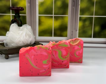 Op de afbeelding: Drie handgemaakte zeepjes met een roze en groene swirl-patroon. De zeep is bezaaid met zwarte zaadjes.