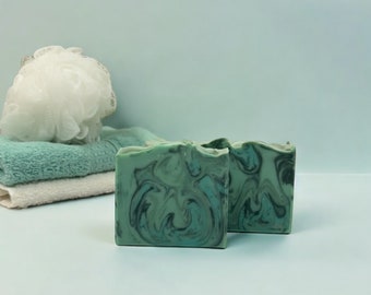 May include: Two bars of green and blue marbled soap. The soap is on a light blue surface.