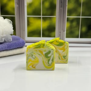 May include: Two bars of handmade soap with a swirl pattern in shades of green, yellow, and white.