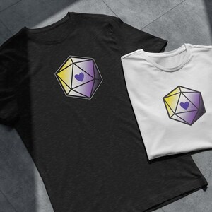 May include: Two t-shirts with a graphic of a yellow, white, and purple dice with a purple heart in the center. The dice is a symbol of the non-binary gender identity.