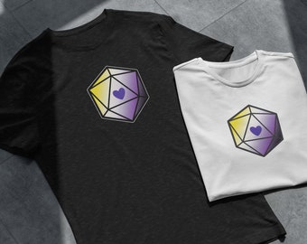 Puede incluir: Dos camisetas con un gráfico de un dado amarillo, blanco y morado con un corazón morado en el centro. El dado es un símbolo de la identidad de género no binaria.
