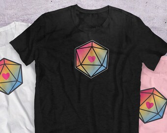 Puede incluir: Tres camisetas con un dado de 20 caras de color arcoíris con un corazón rosa en el centro. Las camisetas son blancas, negras y rosas.