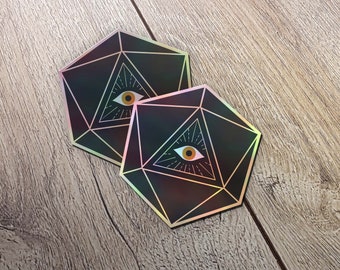 Puede incluir: Dos pegatinas holográficas negras y doradas con un diseño geométrico y un ojo que todo lo ve en el centro. Las pegatinas tienen forma de dado de 20 caras.