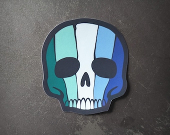 Puede incluir: Una pegatina de una calavera blanca con rayas azules, verdes y blancas. La calavera tiene cuencas de los ojos negras y una sonrisa blanca.