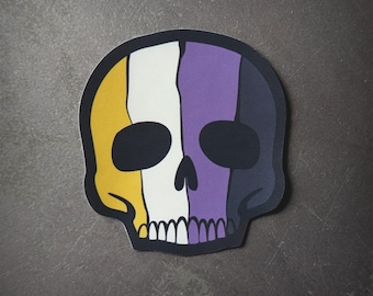 Puede incluir: Una pegatina de calavera negra y blanca con un esquema de color amarillo, blanco y morado. La calavera está estilizada con un diseño simple y es un símbolo popular de la comunidad no binaria.