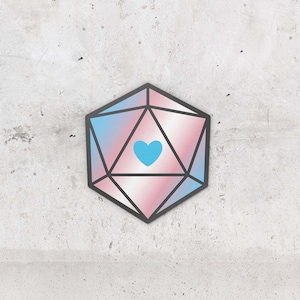 Op de afbeelding: Een 20-zijdige dobbelsteen ontworpen als een transgender pride-vlag in roze, blauw en wit met een blauw hart in het midden.