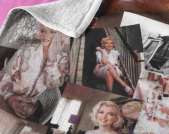 May include: A plush throw blanket featuring a collage of Marilyn Monroe photographs in various poses. The blanket is draped over a bed with pink sheets and a patterned pillow. The images are in both color and black and white.