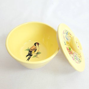 Peut inclure: Un bol en céramique jaune avec un couvercle. Le bol est décoré d'un oiseau peint sur une branche. Le couvercle est orné d'un motif floral.