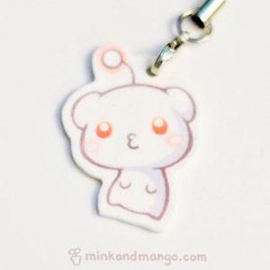 May include: White cartoon character keychain with orange eyes and a pink blush. The character has a small antenna on top of its head and is wearing a silver chain.