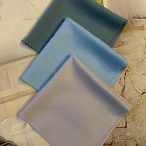 Op de afbeelding: Drie stofstalen in verschillende tinten blauw. De stalen zijn in een driehoekige vorm gerangschikt, met de donkerste blauwe tint bovenaan en de lichtste blauwe tint onderaan.