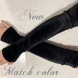 May include: A pair of black velvet arm warmers. The arm warmers are long and reach to the elbow. The text "New" and "Match color" is written on the white surface.