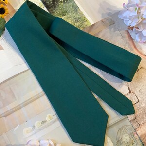 May include: A dark green necktie with a pointed end. The tie is folded in half and laid flat on a surface.