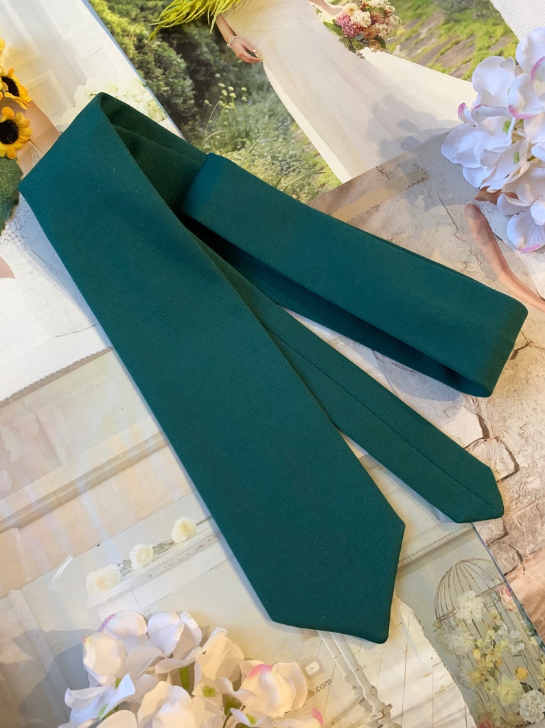May include: A dark green necktie with a pointed end. The tie is folded in half and laid flat on a surface.