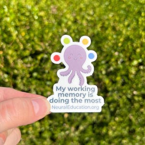 May include: A sticker featuring a purple octopus with colorful circles on its head. The sticker has the text "My working memory is doing the most" and "NeuralEducation.org". The sticker is held against a green, blurred background.