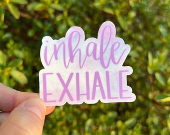 May include: A sticker with a watercolor background in shades of purple and blue. The sticker has the words "inhale exhale" written in purple.