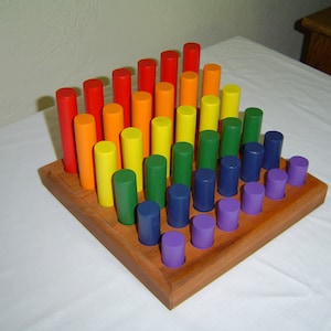 May include: A wooden rainbow stacking toy with colorful wooden cylinders of different lengths. The toy is arranged in a pyramid shape on a wooden base.