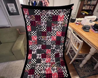 May include: A black and red patchwork quilt with a snake pattern. The quilt is made of different fabrics and has a black border.
