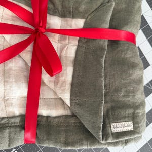 May include: A green and white quilted blanket tied with a red ribbon. The blanket has a label that says "Blanket Babie".