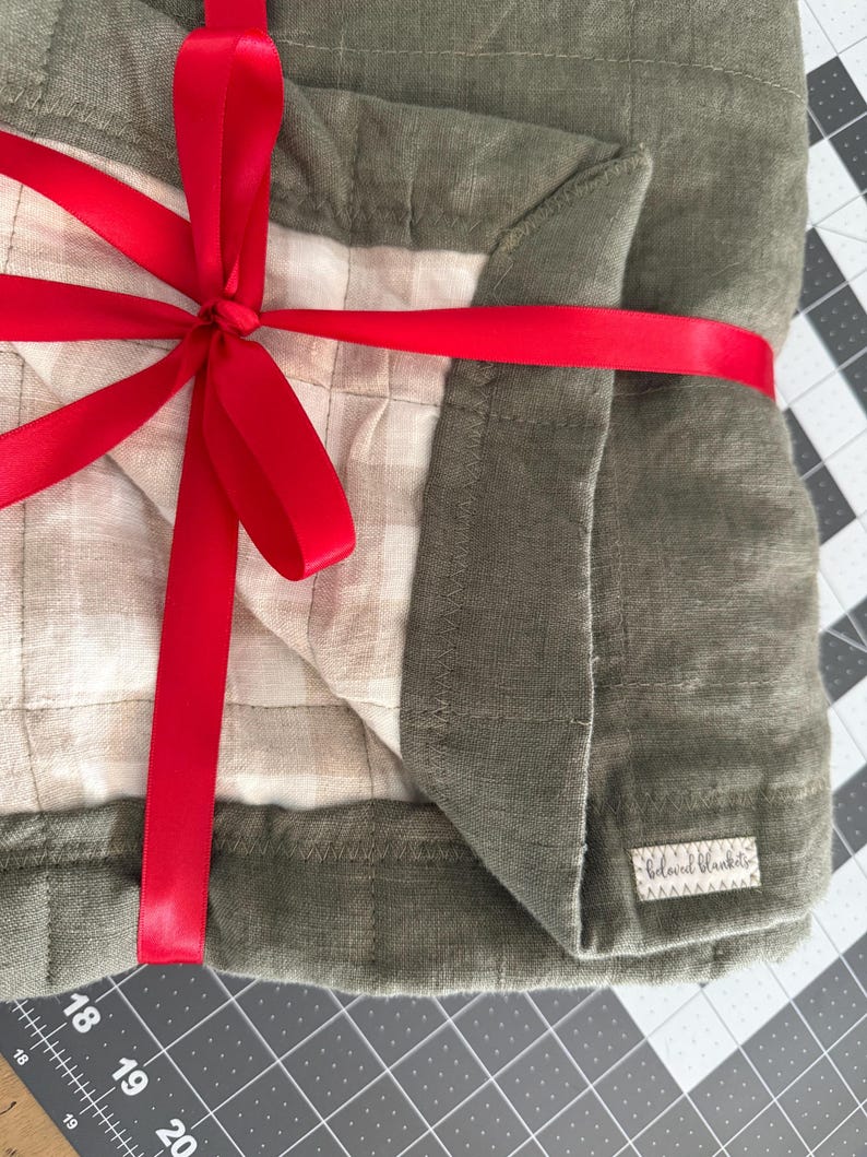 May include: A green and white quilted blanket tied with a red ribbon. The blanket has a label that says "Blanket Babie".