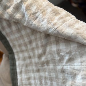 May include: A beige and white checkered throw blanket with a green border. The blanket is made of a soft, linen fabric and has a quilted design.
