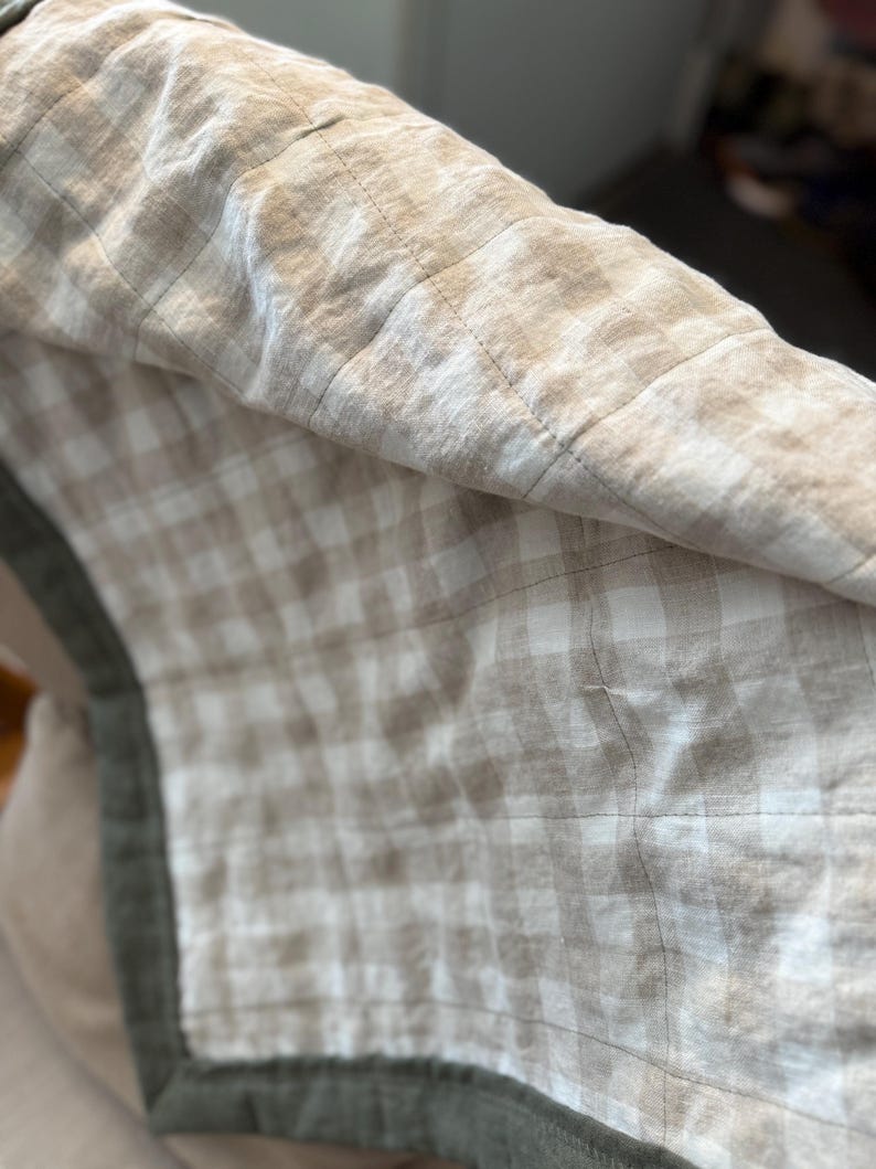May include: A beige and white checkered throw blanket with a green border. The blanket is made of a soft, linen fabric and has a quilted design.