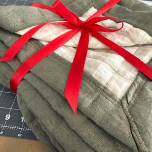 May include: Stack of five olive green linen dish towels tied with a red ribbon.