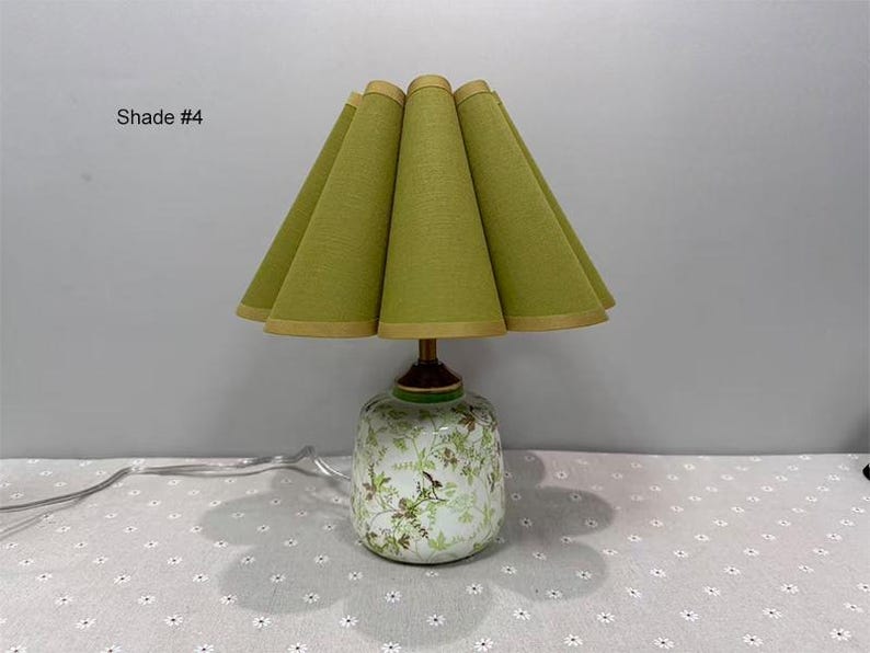 May include: A decorative table lamp with a green lampshade and a floral patterned base. The lampshade is a light green color with a gold trim. The base is white with green and brown floral designs. The text "Shade #4" is in the upper left corner.