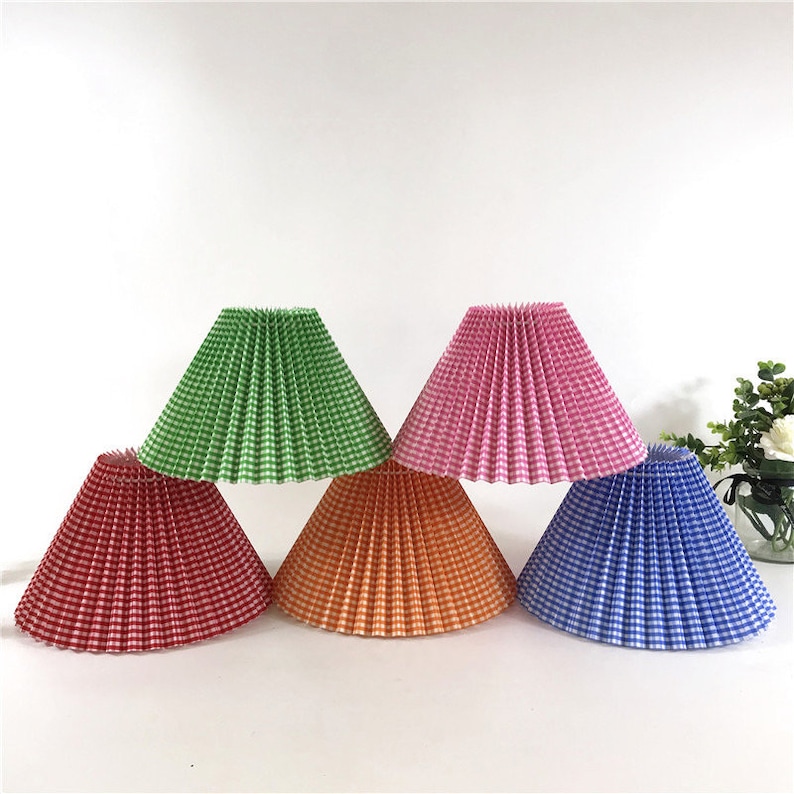 May include: Five lampshades in different colors with a checkered pattern. The lampshades are pleated and have a conical shape. The colors are green, pink, red, orange, and blue.