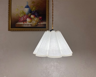 May include: A white fabric lampshade with a pleated design hangs from a ceiling fixture. The lampshade is illuminated, casting a soft glow.